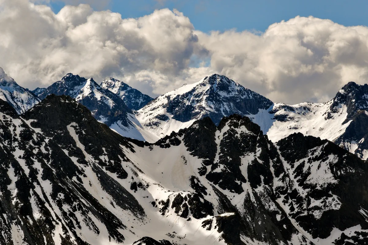 Schroffe Felsgipfel mit Schneefeldern, darüber Quellwolken und blauer Himmel