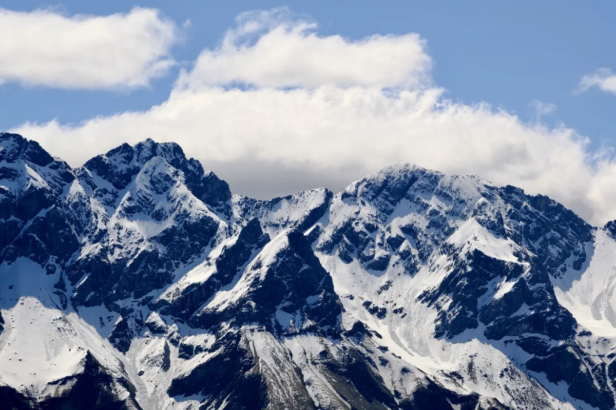 Nahaufnahme eines verschneiten Felsgrats, dahinter eine einzelne Wolkenbank vor blauem Himmel
