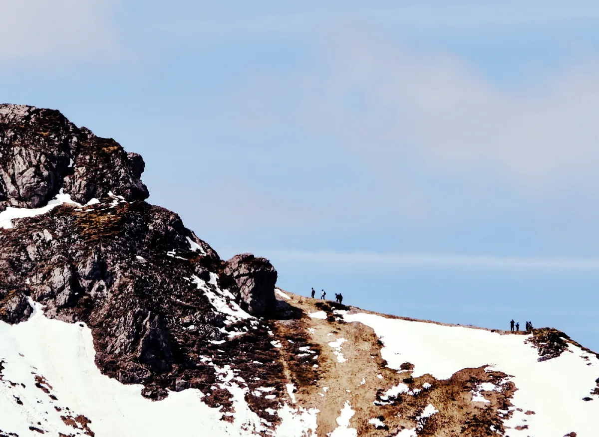 Kleine Wandergruppen als Silhouetten auf einem schneebedeckten Grat neben einer Felsnase