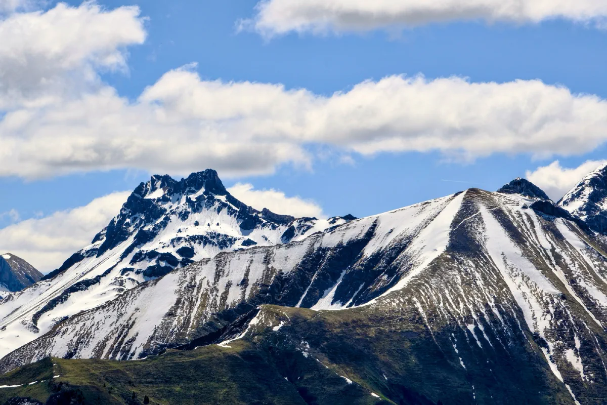 Bergkette mit Schneefeldern in den Flanken, darüber weiße Quellwolken am blauen Himmel