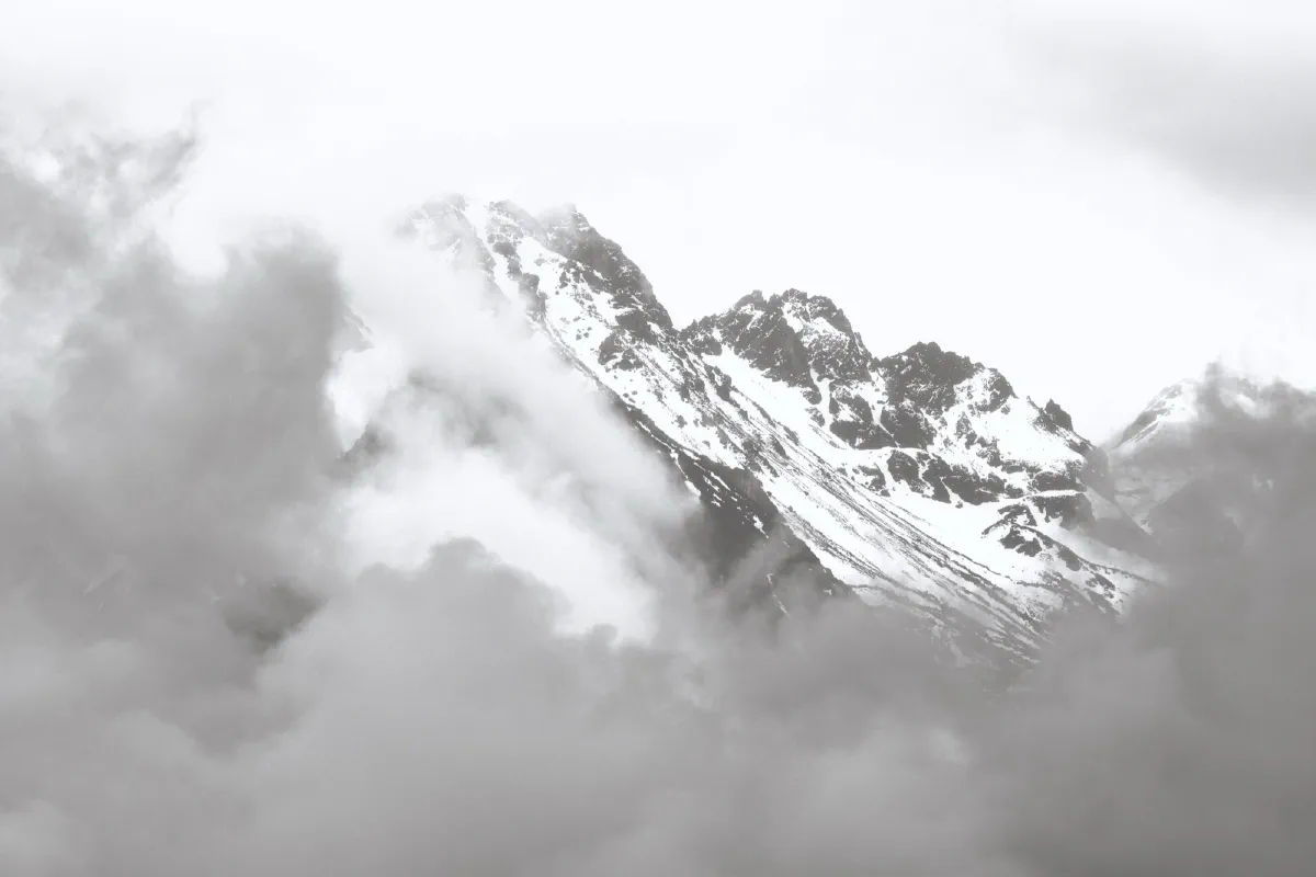 Verschneiter Berggipfel, fast vollständig von Wolken verhüllt, nahezu monochrom