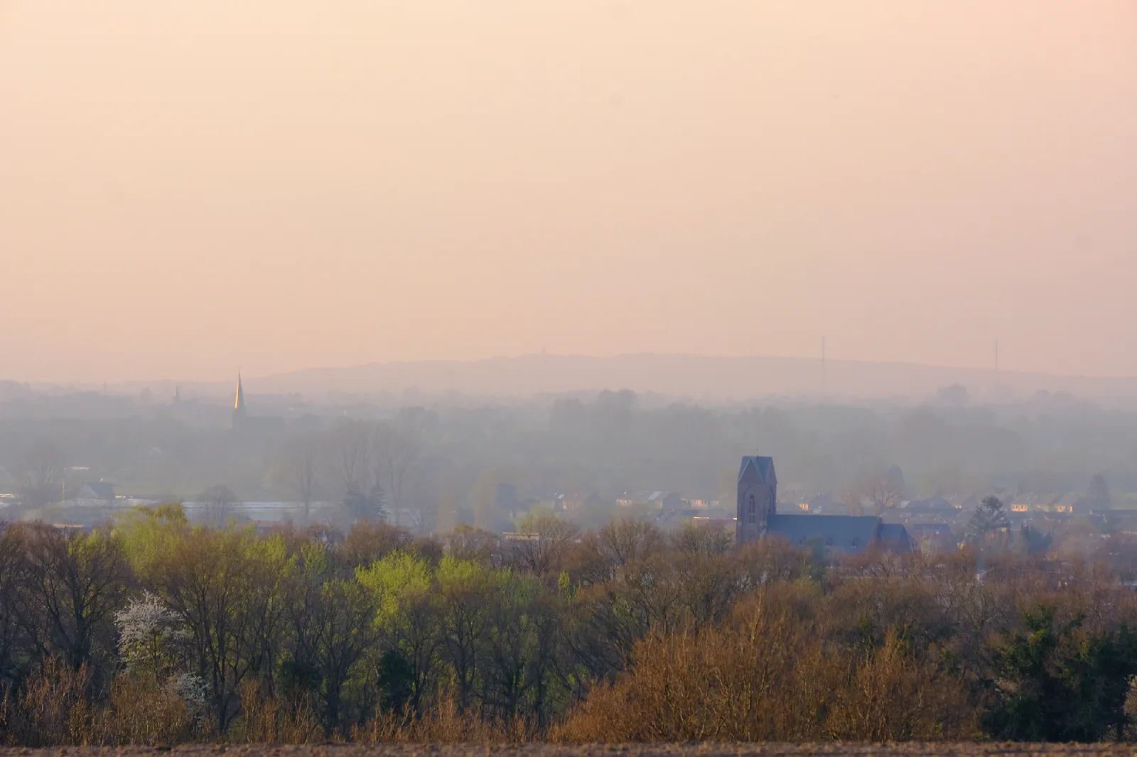 Dunstiger Blick über eine Ortschaft, ein Kirchturm und ein Backsteinturm zeichnen sich im rosafarbenen Licht ab