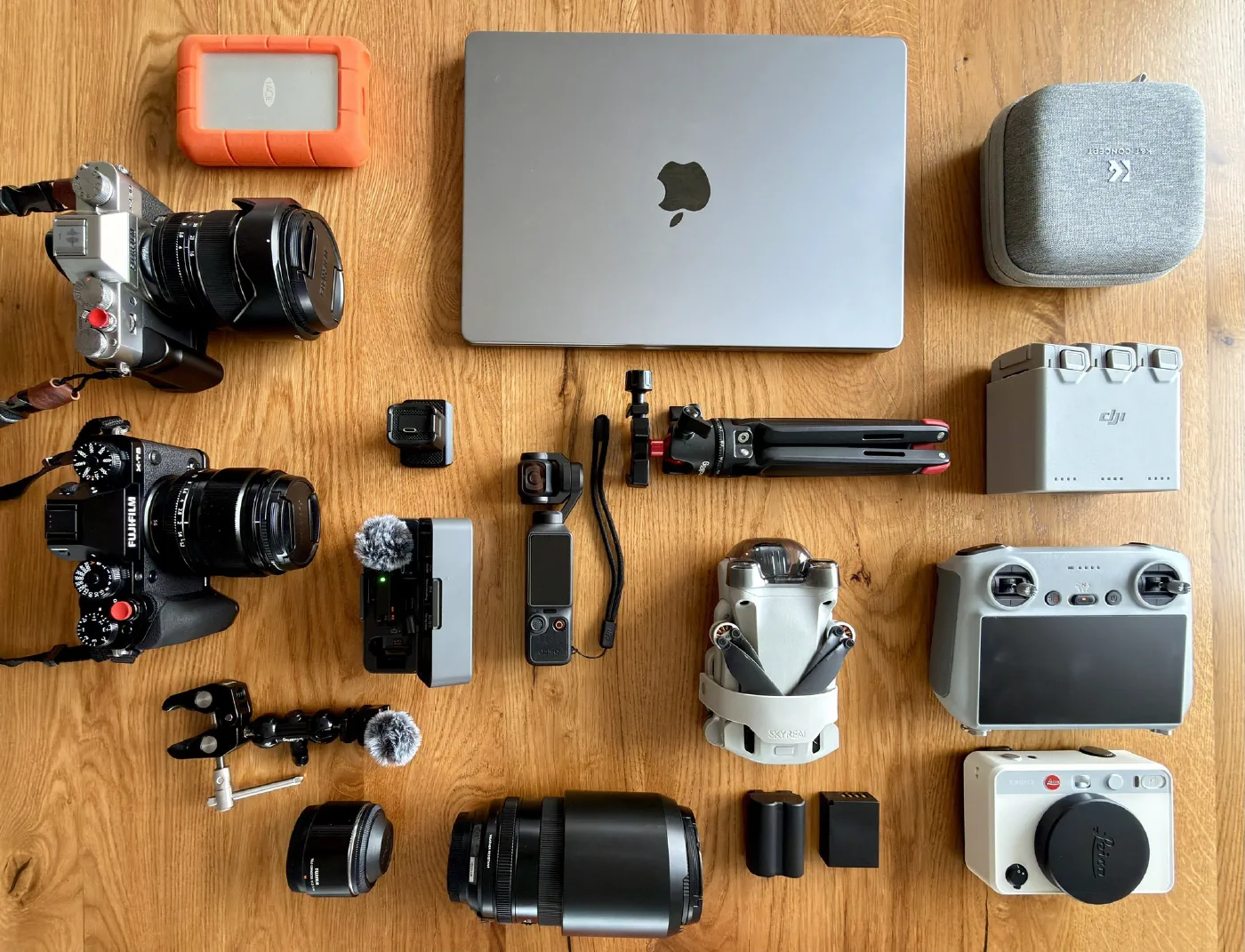 Die Fotoausrüstung auf einer Eichenplatte: zwei Fujifilm-Bodys mit Objektiven, eine DJI-Drohne, Osmo Pocket, Mikrofon, MacBook und eine Leica Sofort 2